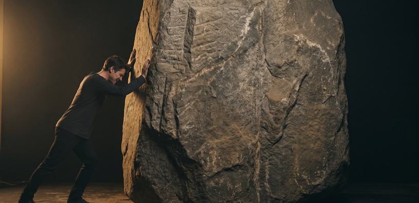 A person braced against the face of a colossal quarried megalith