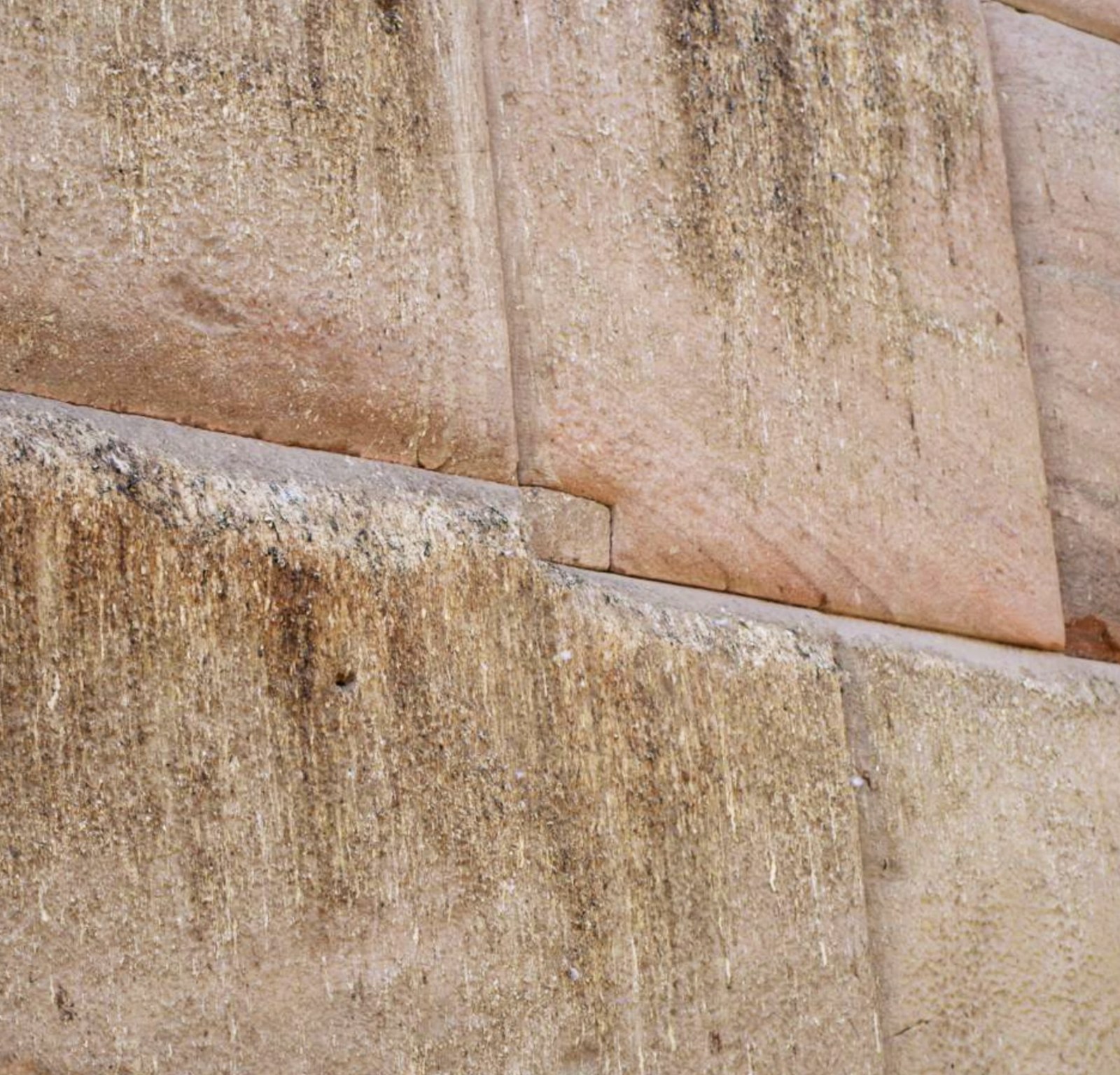 Mini megalith at the Osireion: a small precision-cut stone at the seam between two warm sandstone blocks with bent corners.