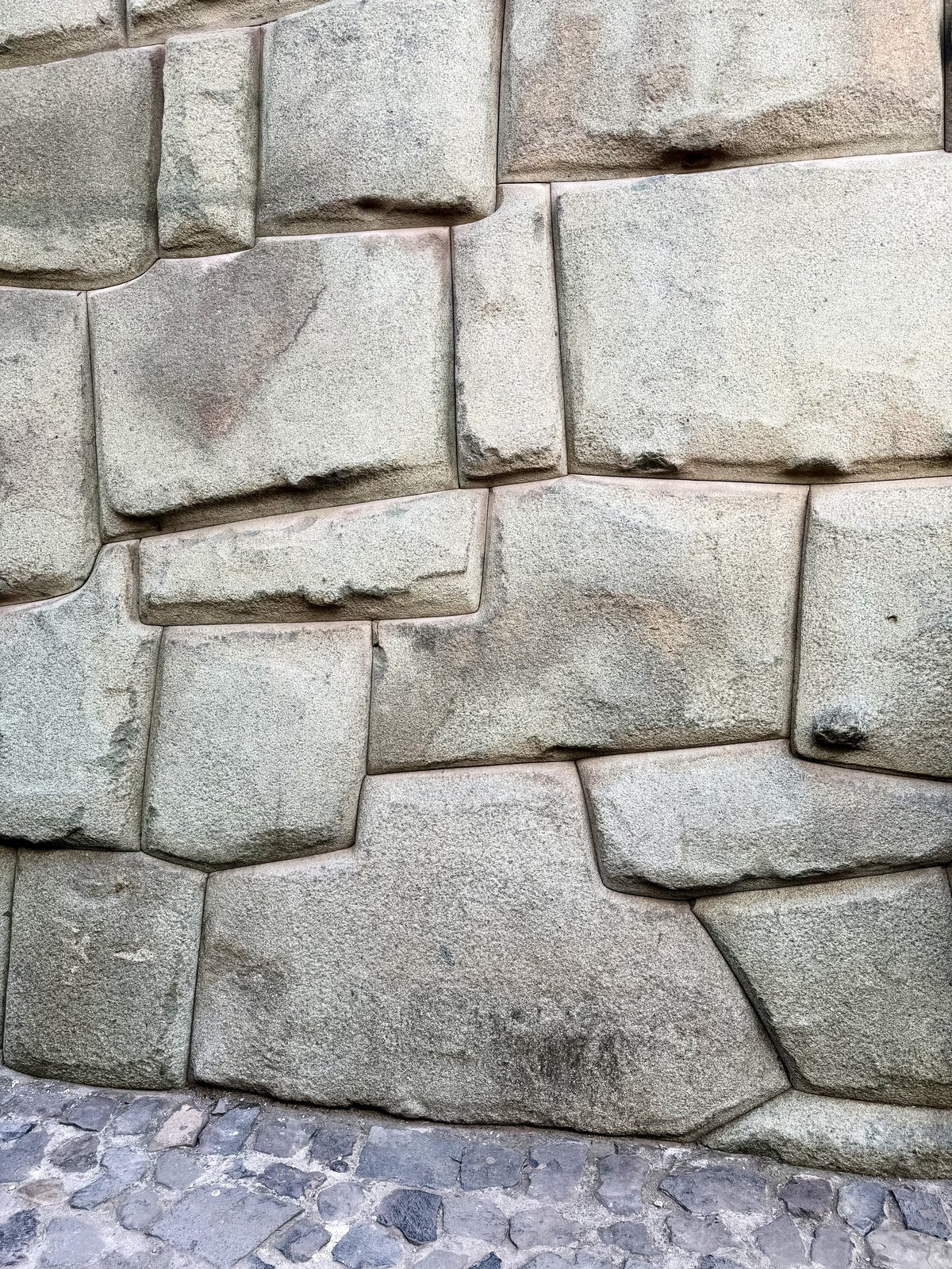 A polygonal Inca wall in central Cusco: many-sided andesite blocks with pillowed faces, each cut to meet its neighbors along tight mortarless seams, above a cobblestone street.