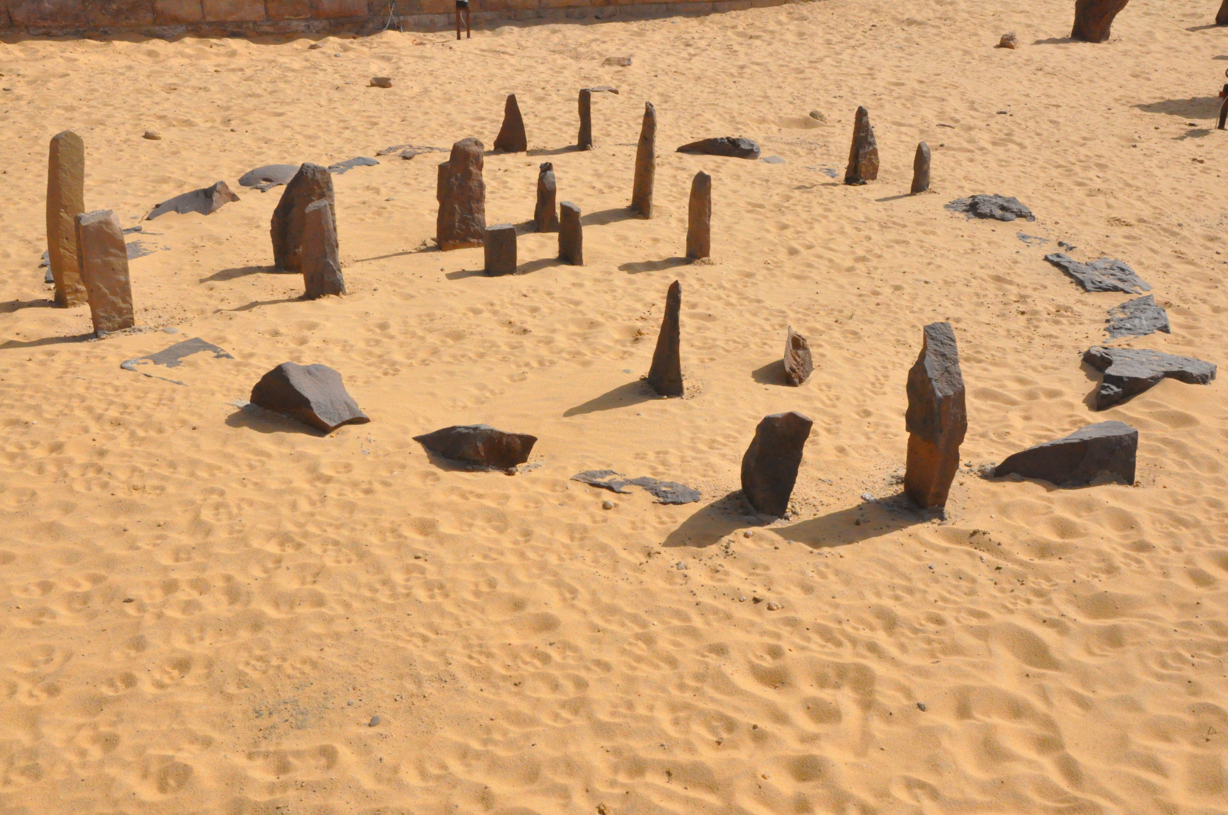 The Nabta Playa calendar circle: standing sandstone slabs arranged in a small ring in the orange desert sand of southern Egypt, with horizon-fixing gate stones aligned to the summer solstice sunrise.