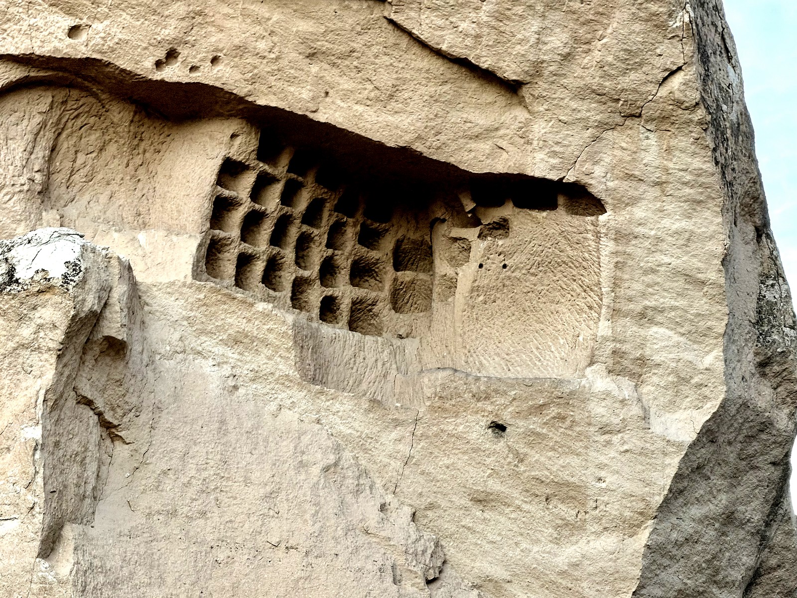 Rock-cut wall at Göreme, Cappadocia, with a precision grid of square chambers cut into the upper face.