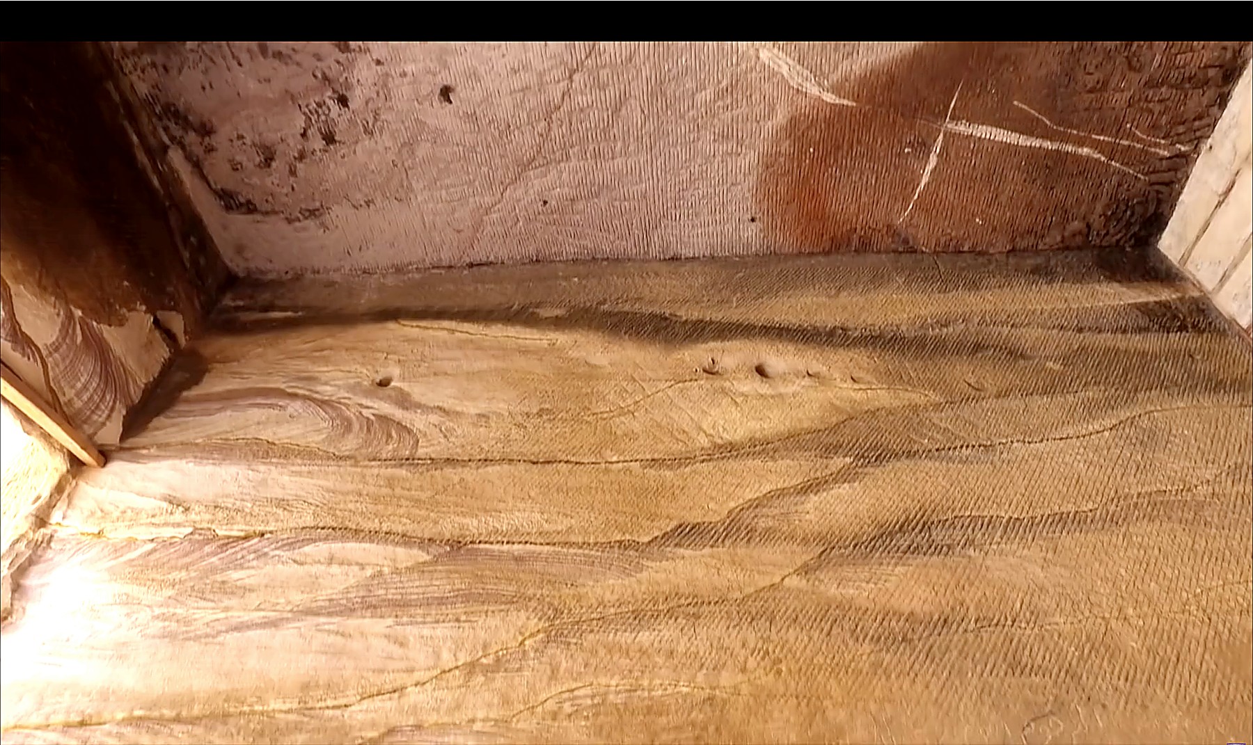 Ceiling of a rock-cut chamber at Little Petra showing prominent parallel diagonal raking marks running uninterrupted across the inverted surface, with the marbled sandstone wall meeting the ceiling visible in the upper corner.