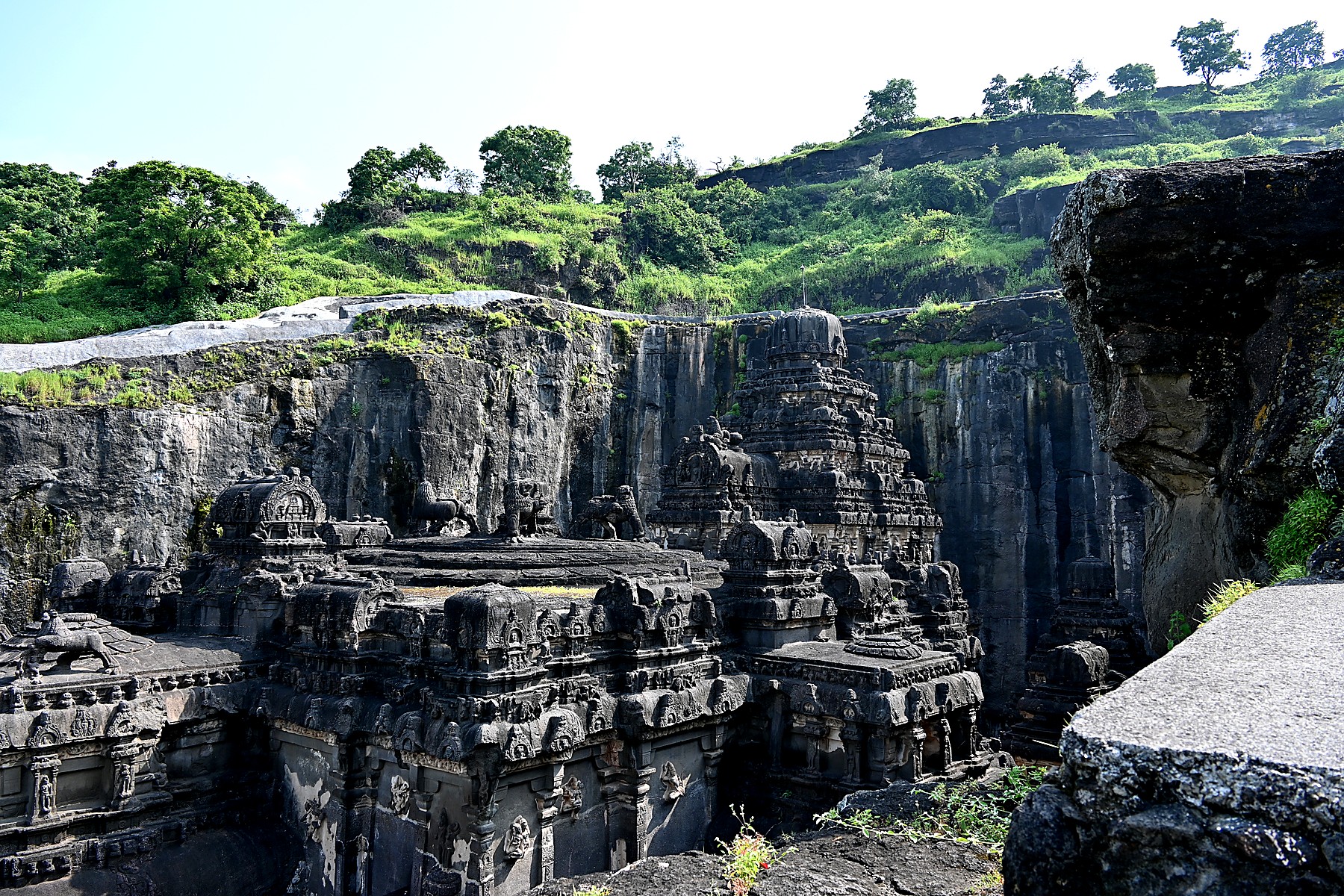 Kailasa Temple at Ellora, viewed from the original cliff face. The temple sits at the bottom of a trench carved straight down through 30 metres of basalt, with the grassy plateau of the original ground level visible at the top of the surrounding cliff.